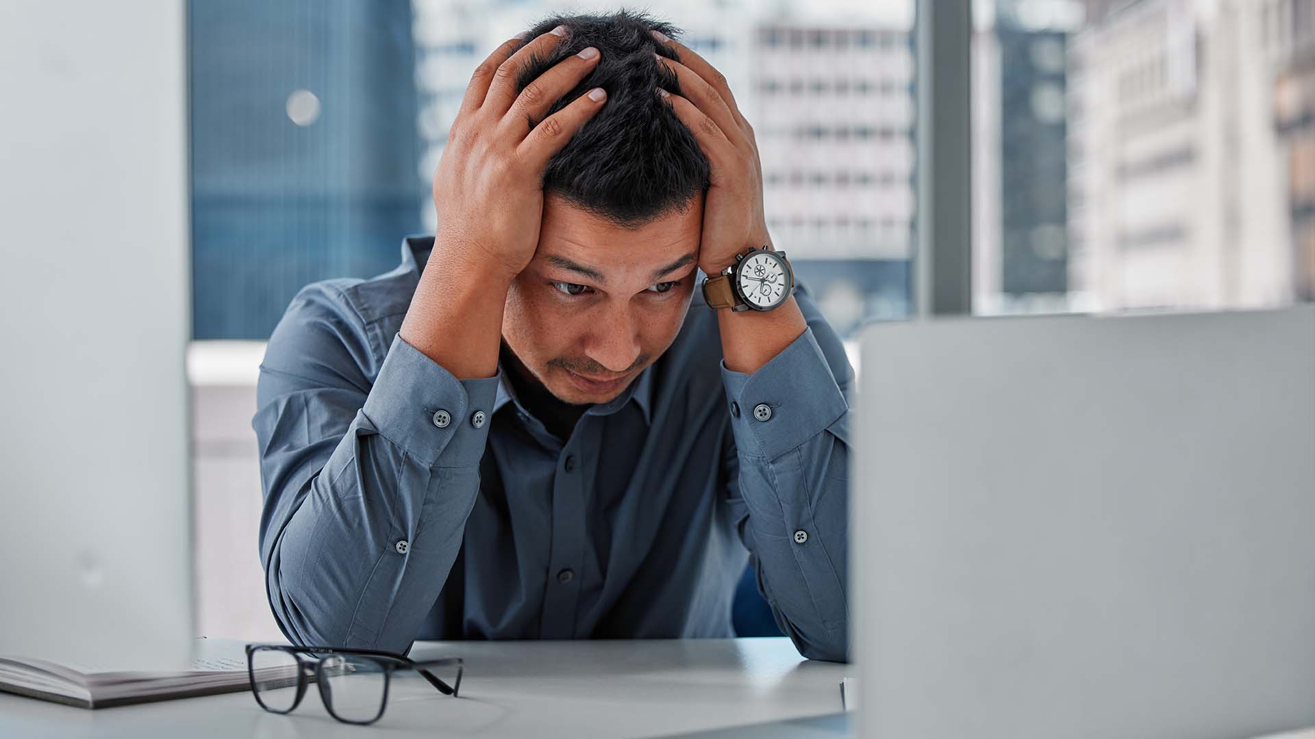 Stressed venture capitalist with head in hands at high-rise office desk