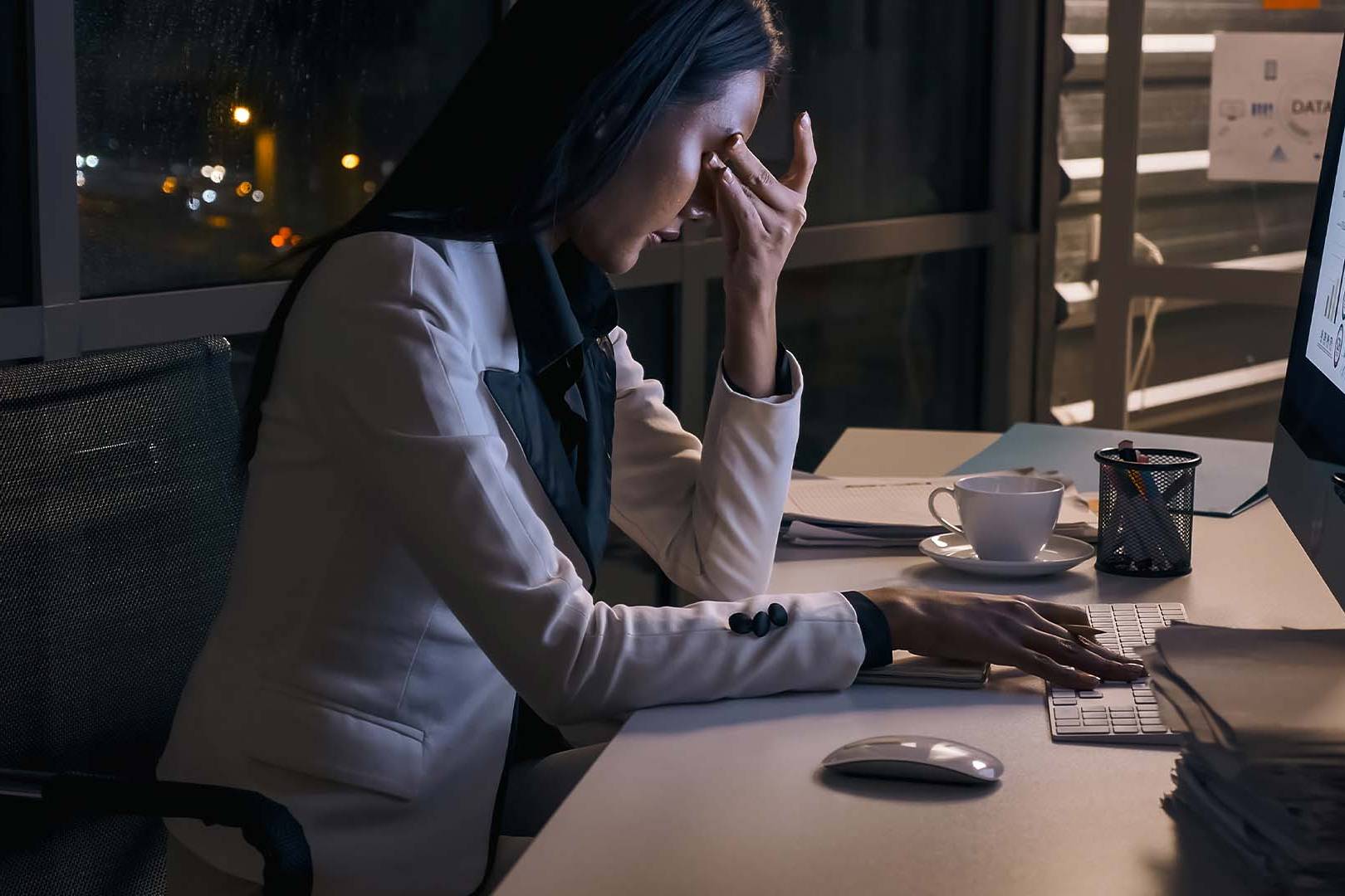 Professional woman working late at night at computer desk showing signs of emotional disconnection and detachment from prolonged work stress