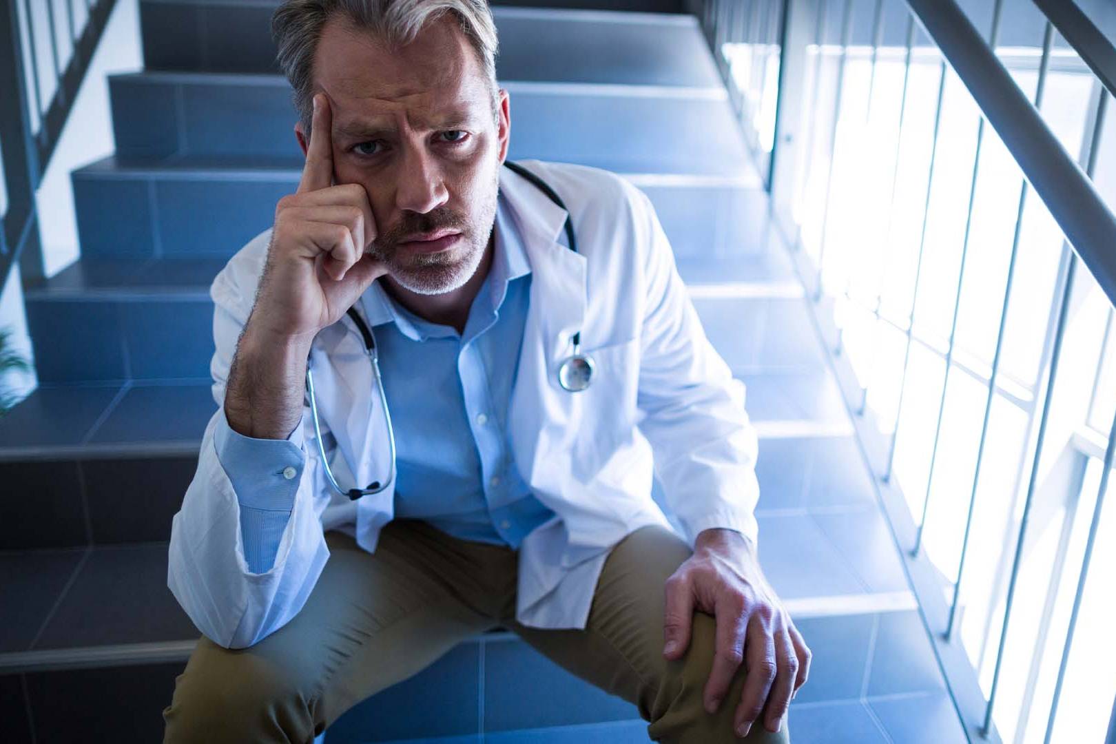 Frustrated doctor in lab coat sitting on stairs, hand on chin in deep thought