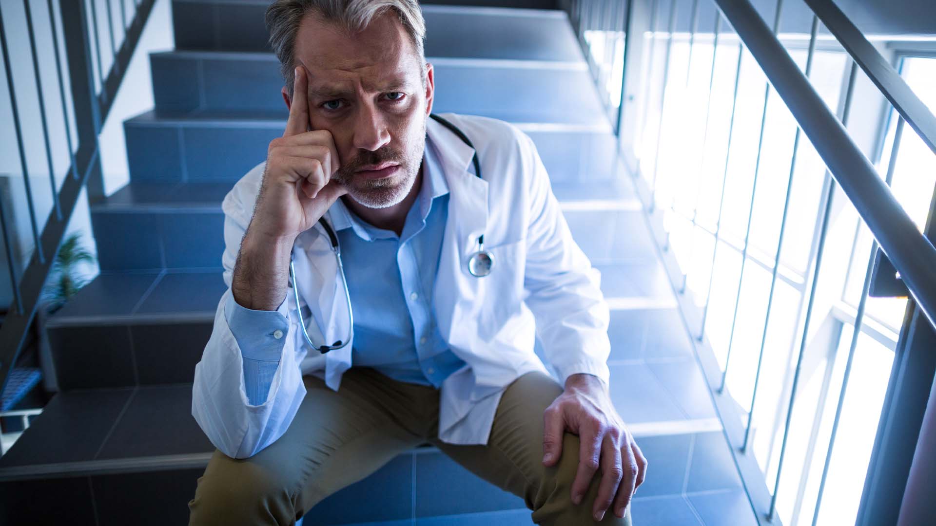 Frustrated doctor in lab coat sitting on stairs, hand on chin in deep thought