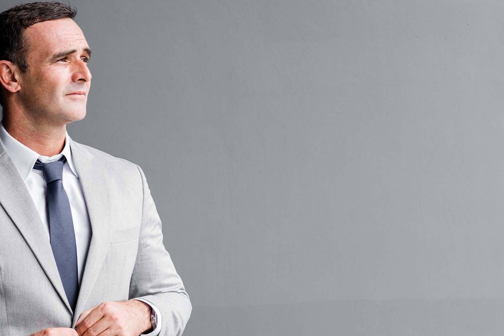Professional man in light gray suit gazing thoughtfully into the distance on a neutral gray background