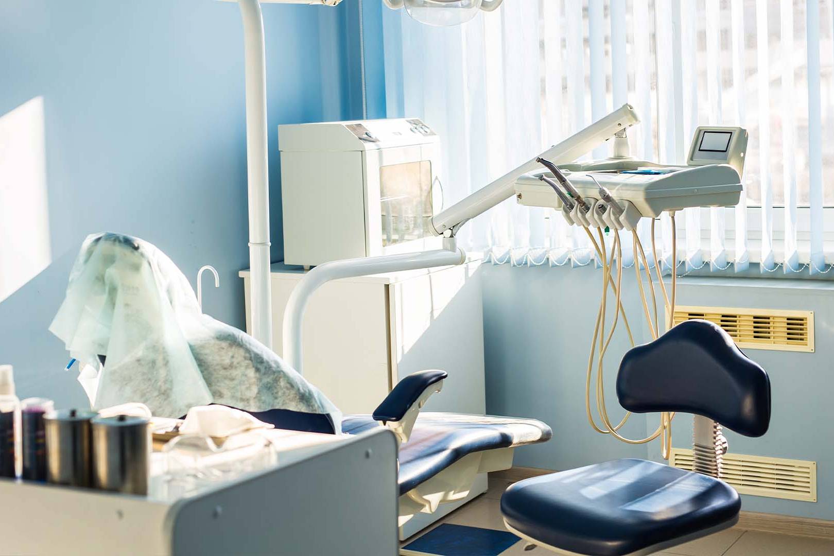 Empty dental clinic room with patient chair, equipment, and natural light