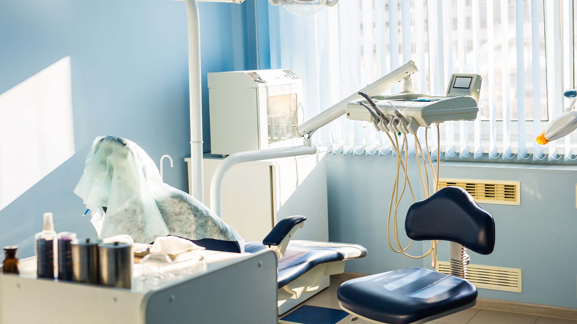 Empty dental clinic room with patient chair, equipment, and natural light