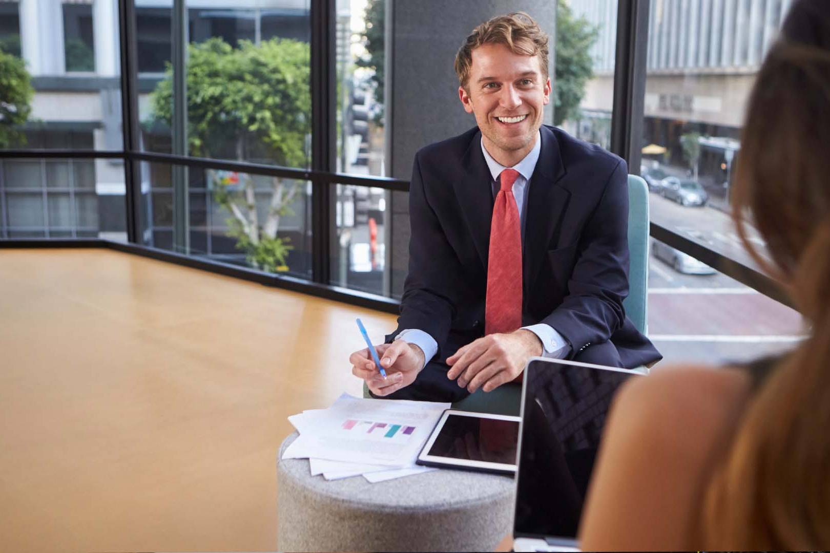 Investment banker in navy suit with red tie reviewing financial charts in downtown Los Angeles high-rise conference room