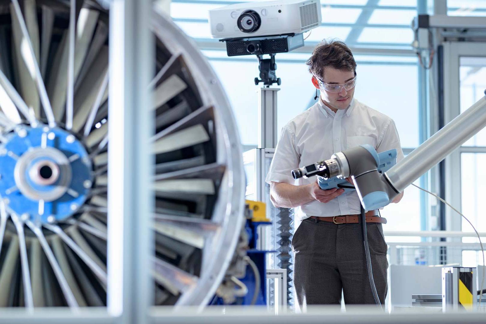 Engineer with glasses collaborating with robotic arm on turbine engine in high-tech lab