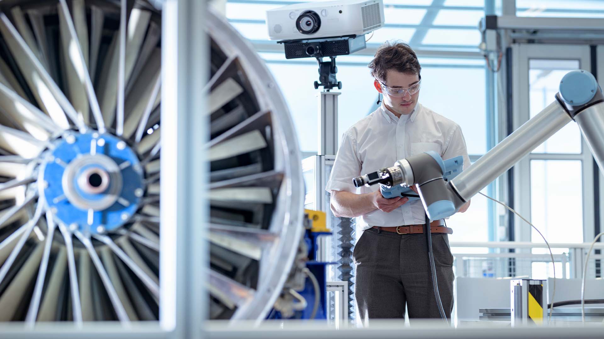 Engineer with glasses collaborating with robotic arm on turbine engine in high-tech lab
