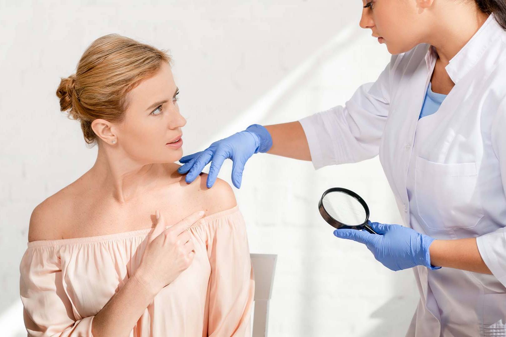 Dermatologist examining patient's skin with magnifying glass in clinical setting