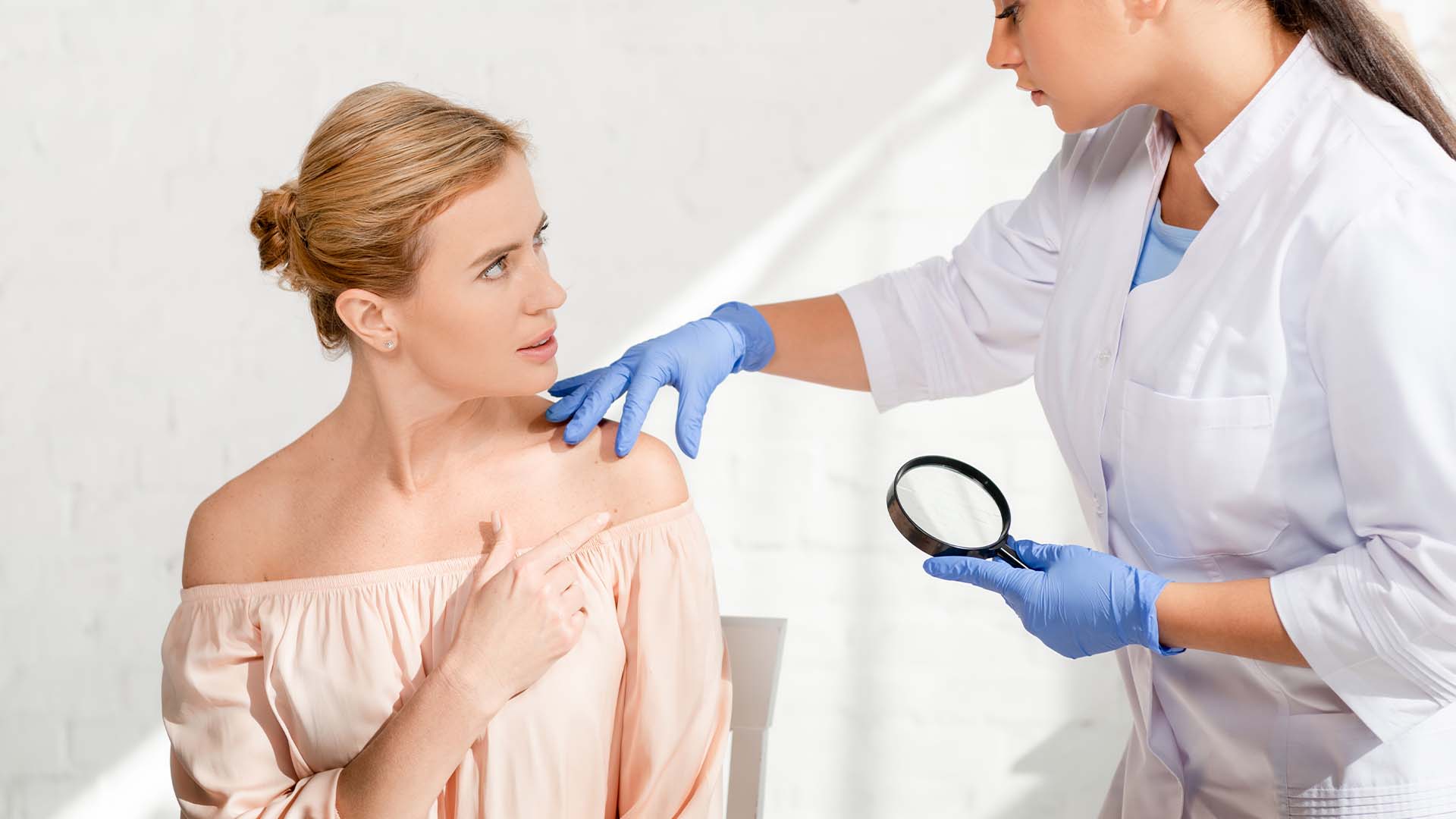 Dermatologist examining patient's skin with magnifying glass in clinical setting
