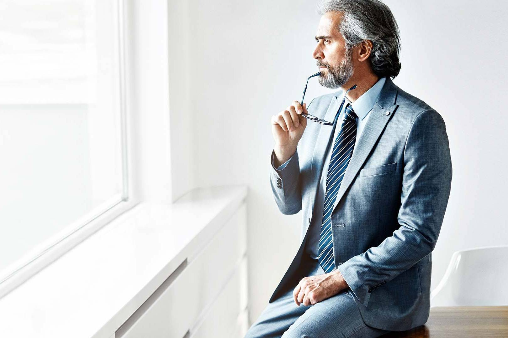 Senior entertainment executive in contemplative pose by window in minimalist office, representing the high-pressure decision-making in Los Angeles entertainment industry