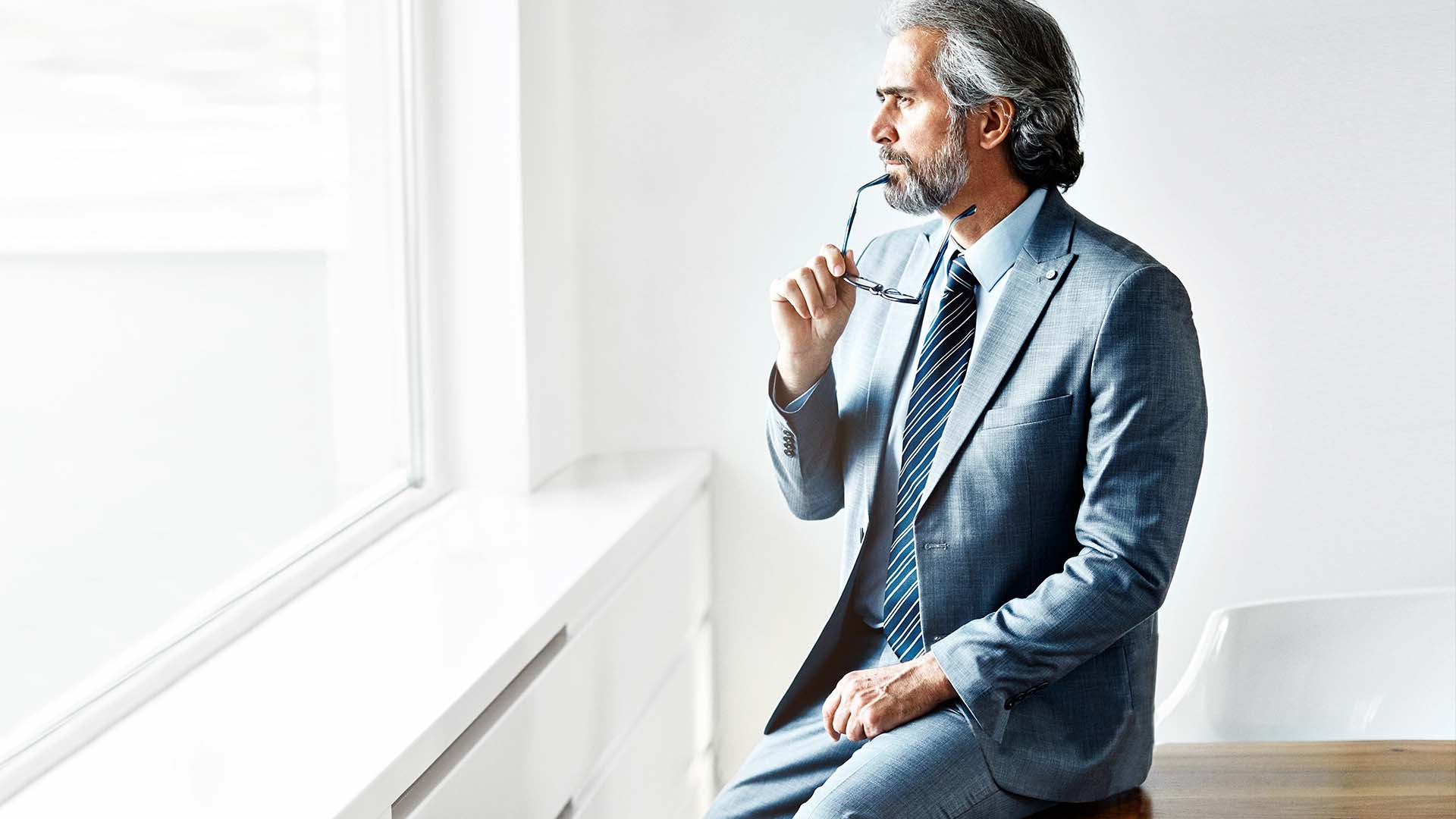 Senior entertainment executive in contemplative pose by window in minimalist office, representing the high-pressure decision-making in Los Angeles entertainment industry