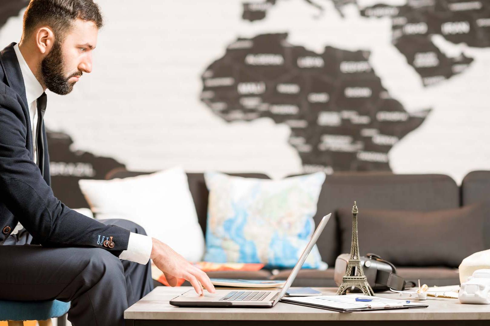 Entrepreneur working intently on laptop with world map in background, representing complete identity fusion with business and global entrepreneurial ambitions