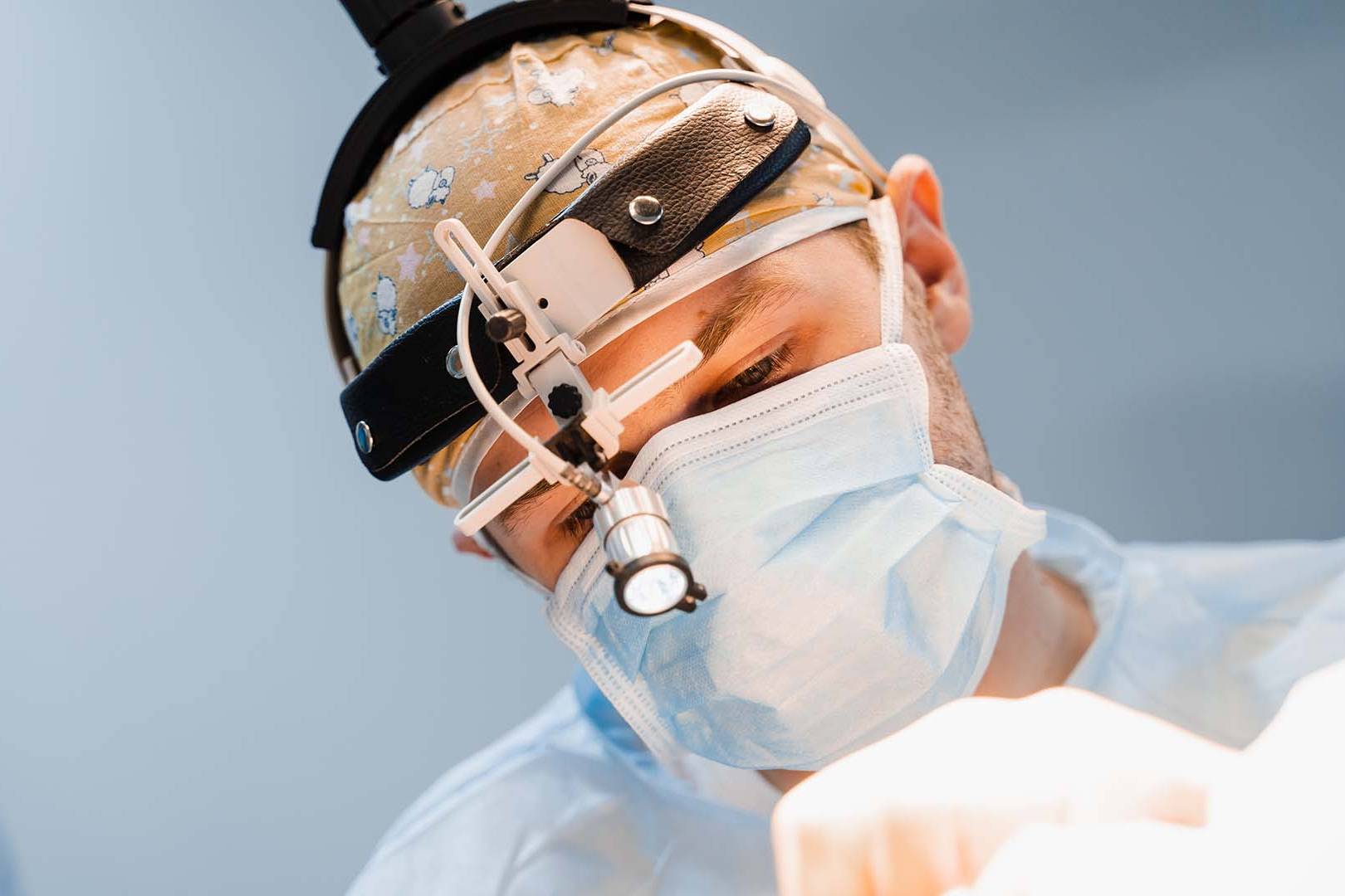 Focused surgeon in headlamp and mask performing precise operation on patient