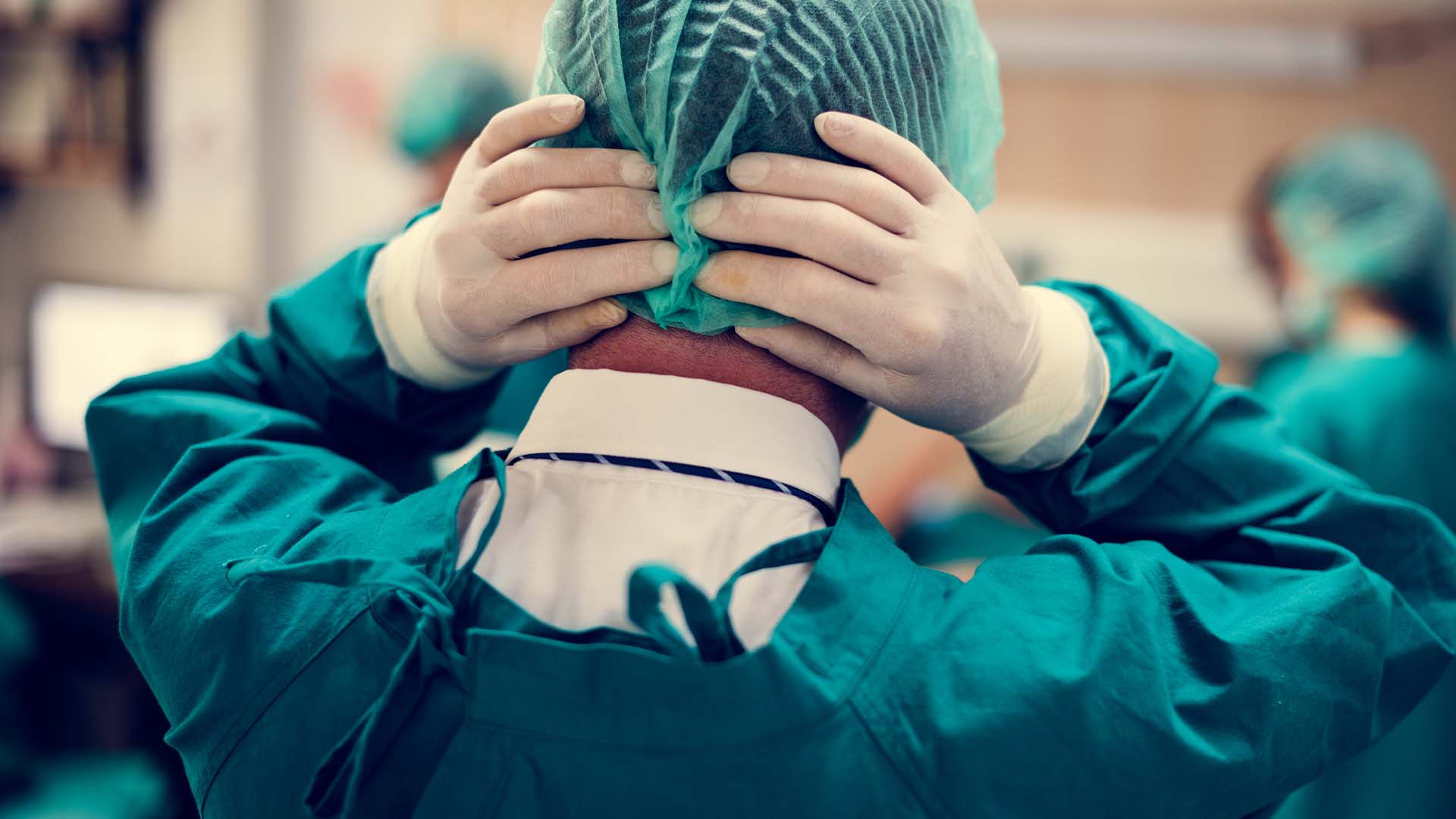 Stressed surgeon in scrubs and cap holding head in frustration during medical procedure
