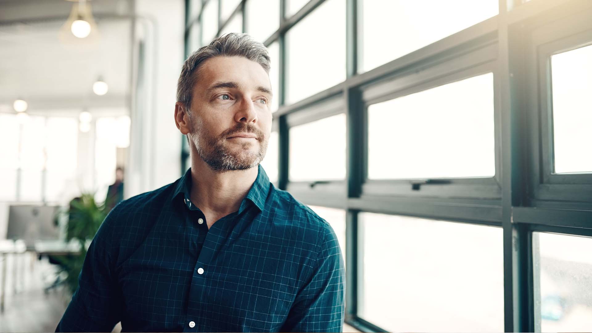 Professional man in contemplative pose looking upward with emotional expression, representing the grief and struggle of infertility while maintaining career demands