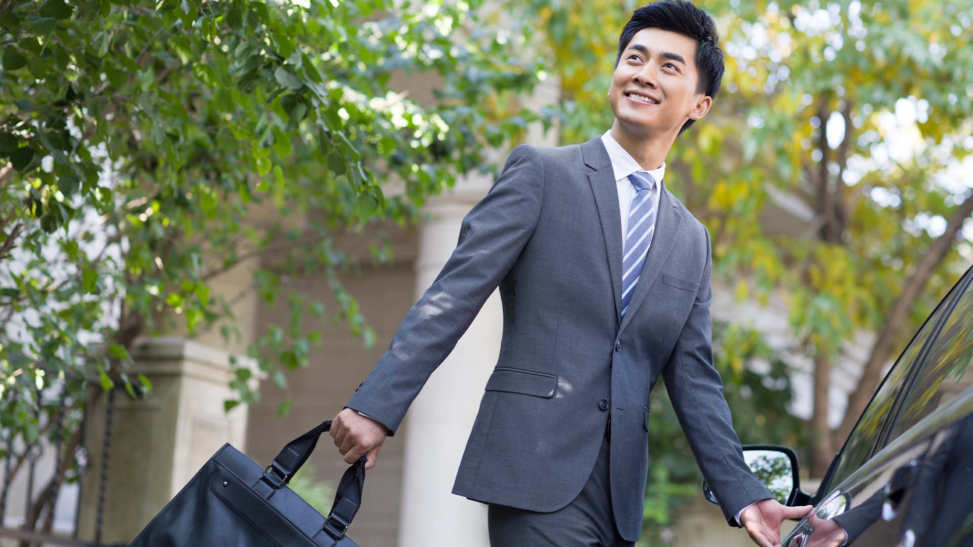 Smiling professional man in suit with briefcase approaching car in outdoor setting