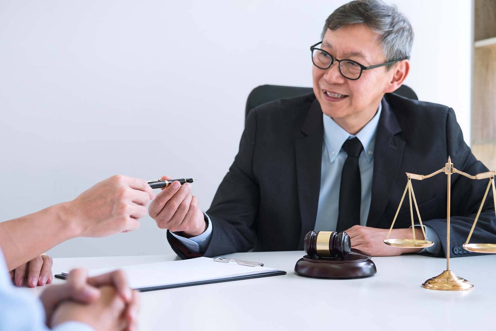 Senior attorney at desk with gavel and scales of justice meeting with client in law office