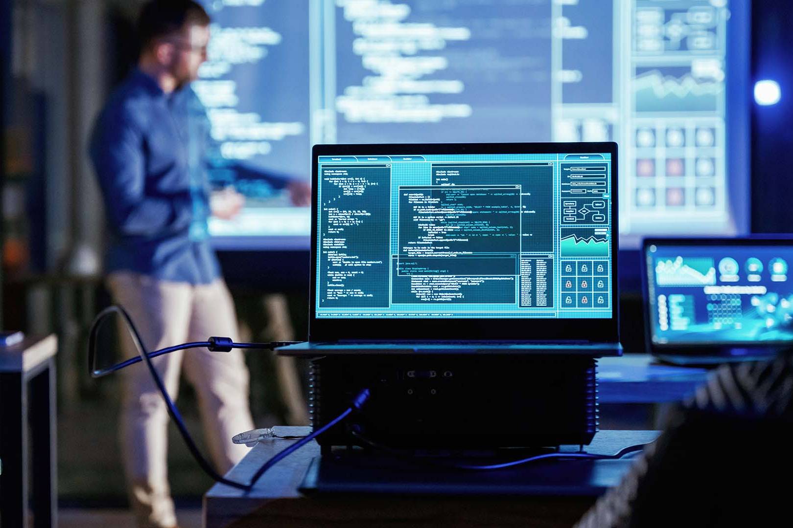 Tech team in dim room analyzing code on multiple screens and large display
