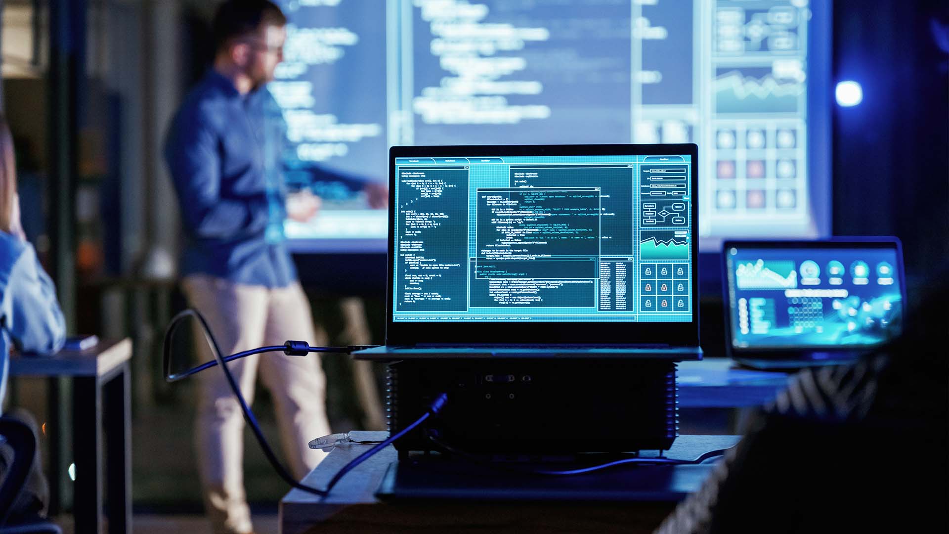Tech team in dim room analyzing code on multiple screens and large display