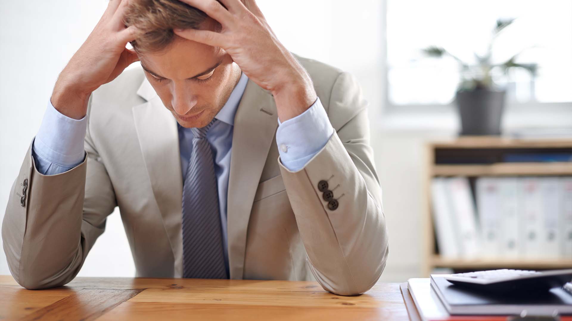 Stressed VC in suit holding head at desk with documents in bright office