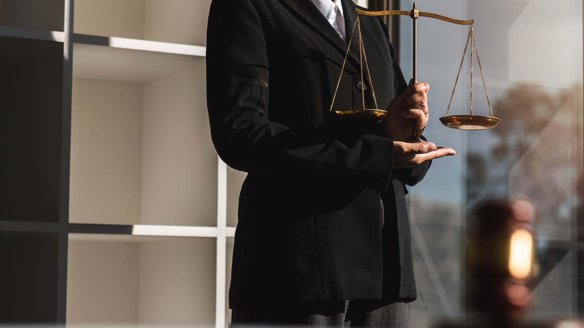 A legal professional in a dark suit holding the scales of justice in a sunlit office, representing the mental health crisis in law.