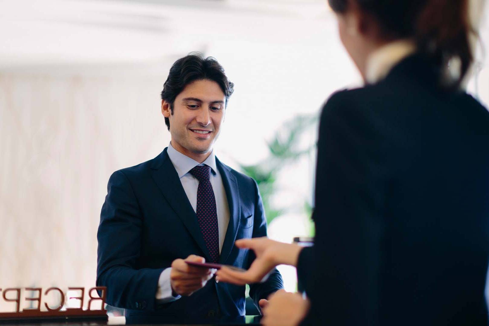 Business professional in a suit receiving a card from a receptionist at a hotel front desk