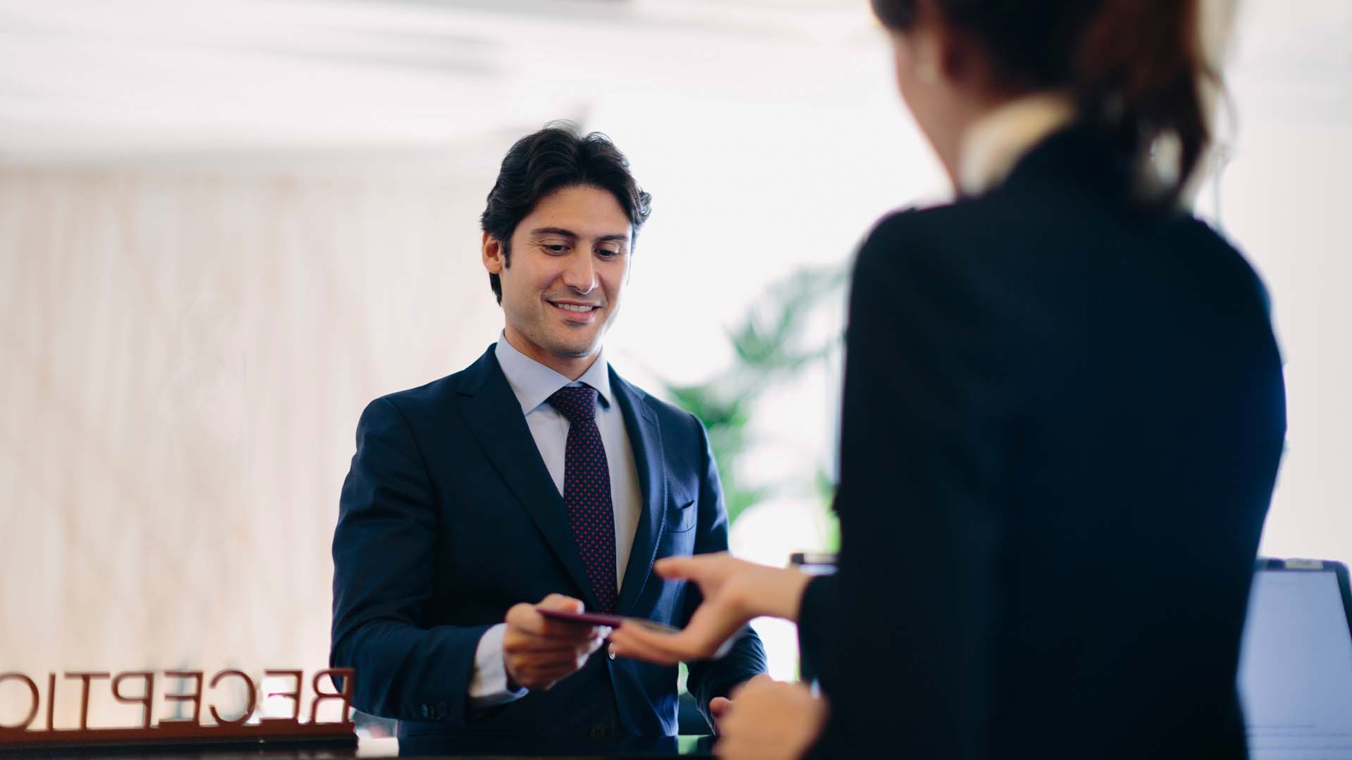 Business professional in a suit receiving a card from a receptionist at a hotel front desk