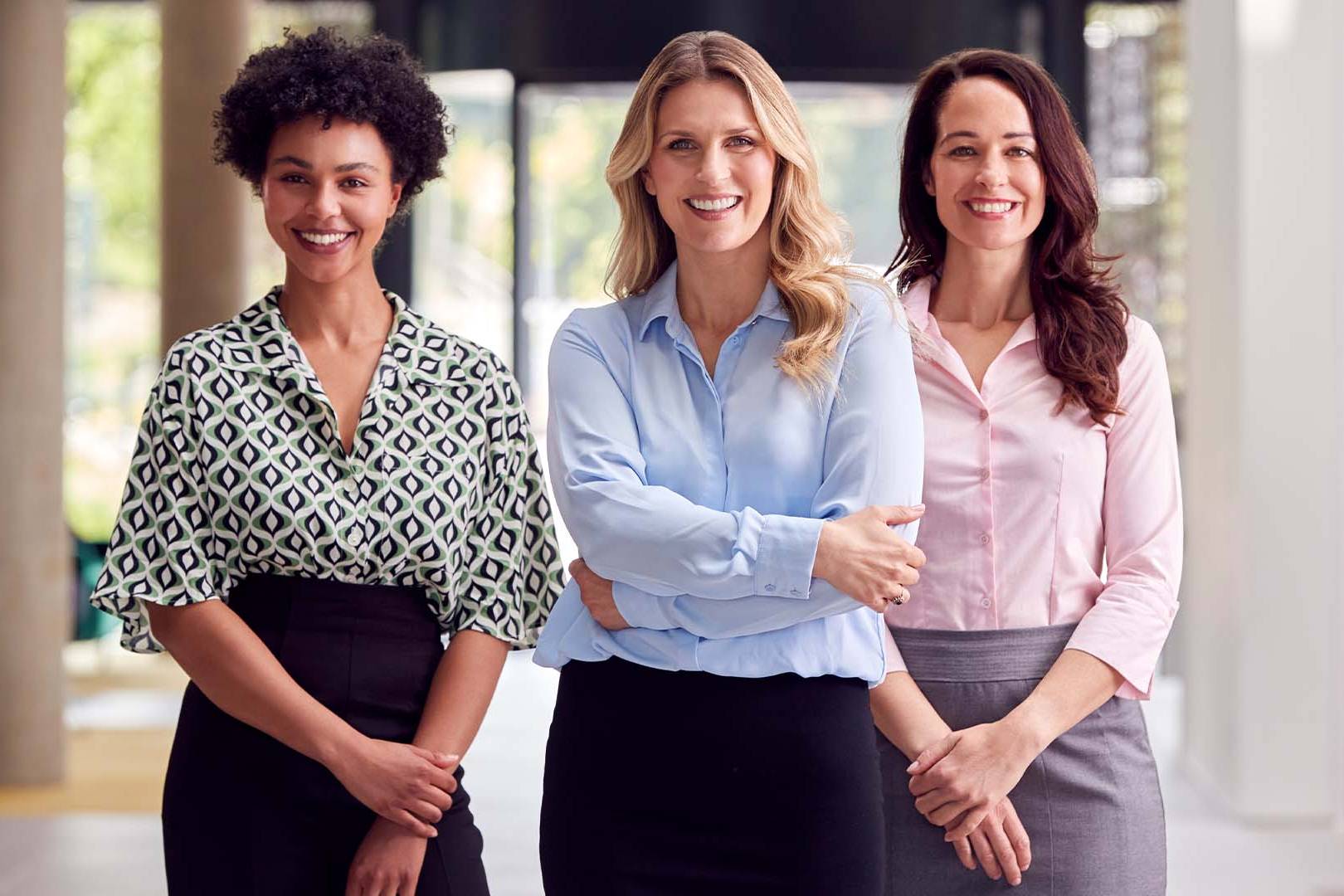 Three diverse female attorneys standing confidently together in a modern law office setting.