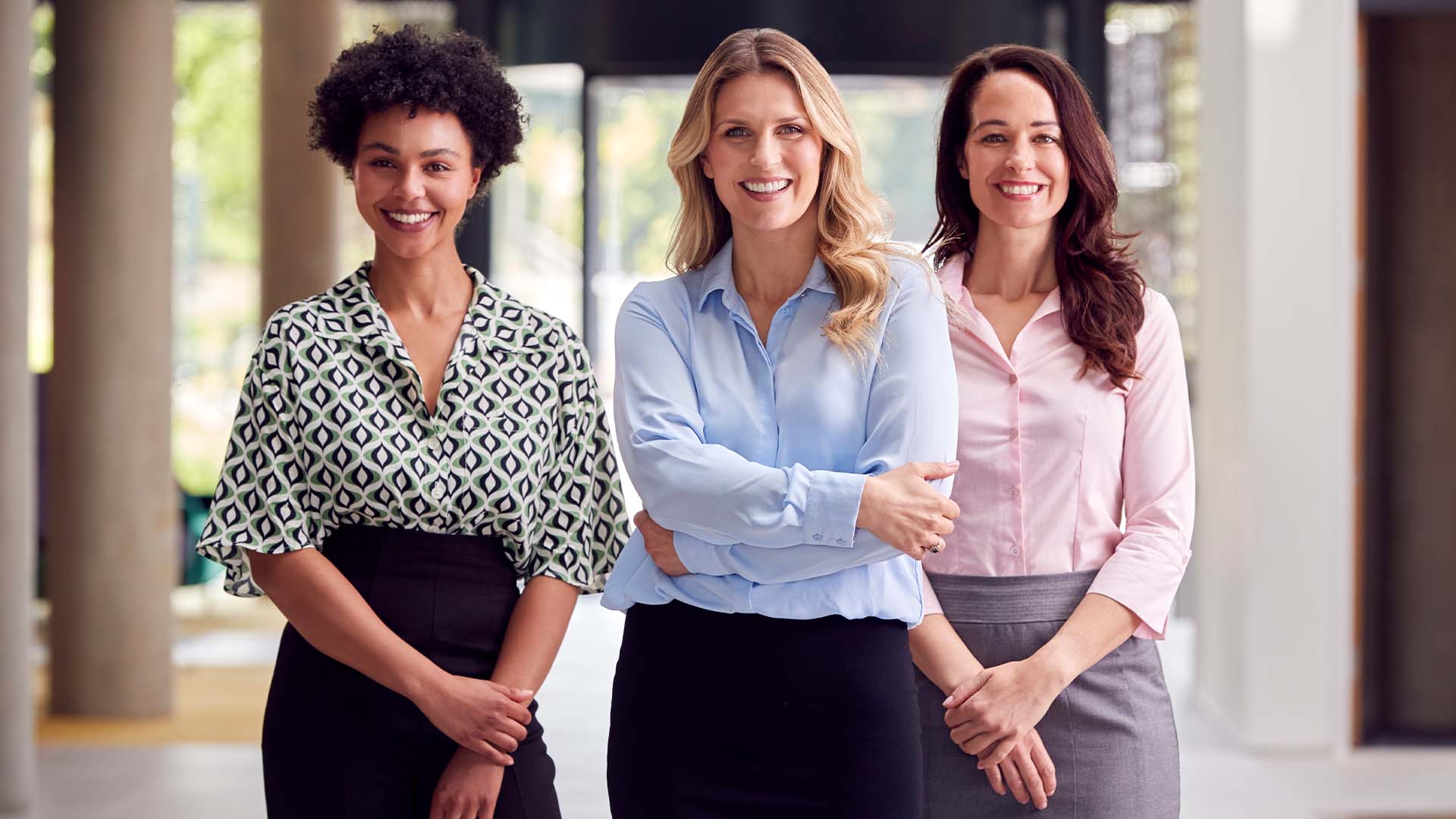 Three diverse female attorneys standing confidently together in a modern law office setting.