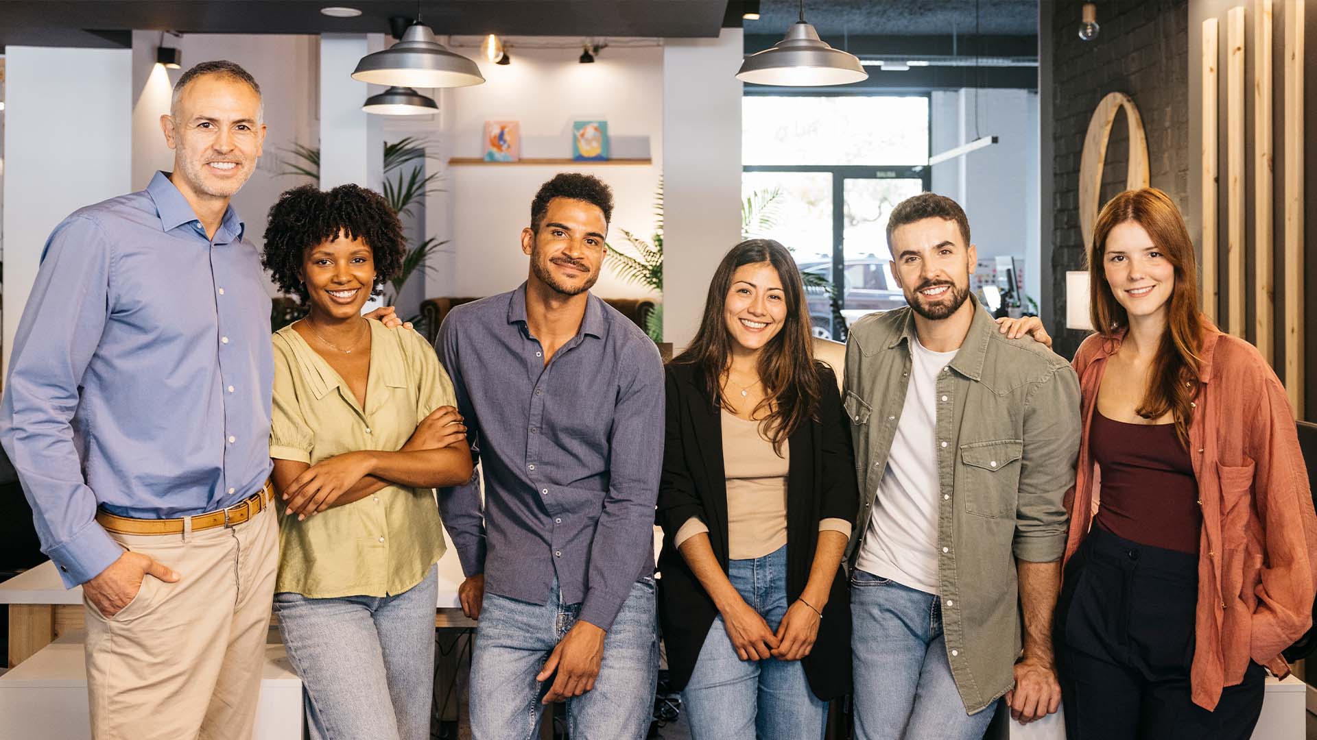 Diverse group of six smiling coworkers standing together in a modern startup office space