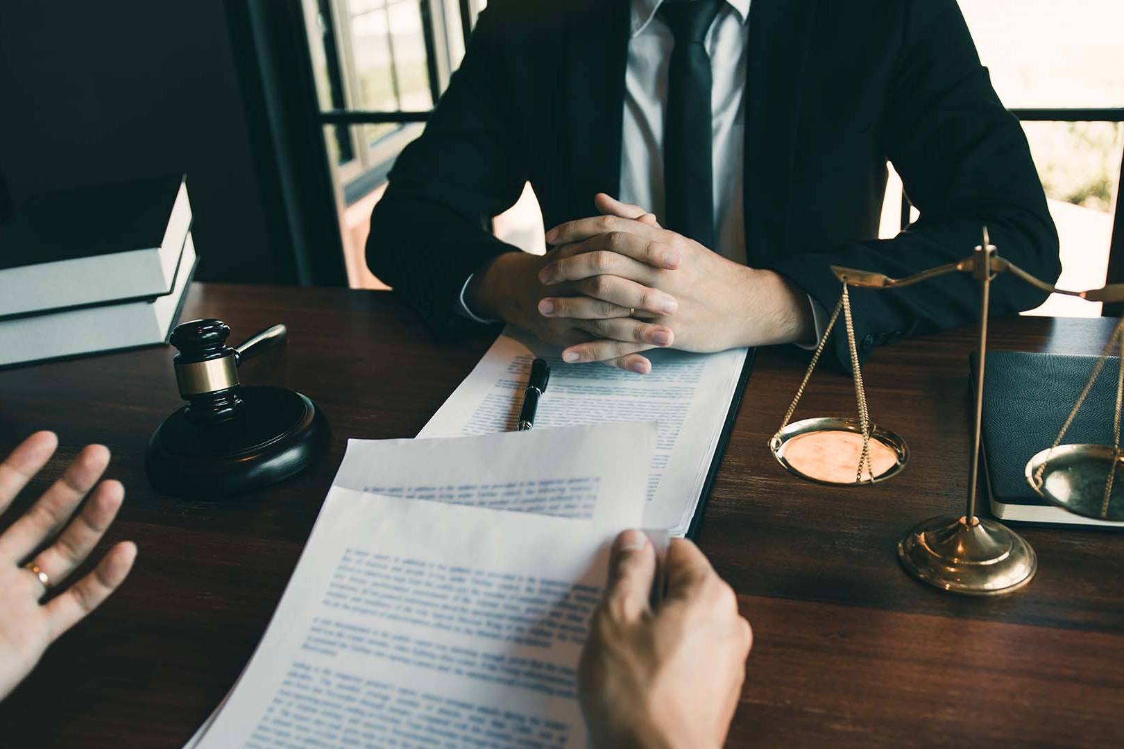 Professional legal consultation with lawyer and client reviewing documents at wooden desk with gavel and scales of justice