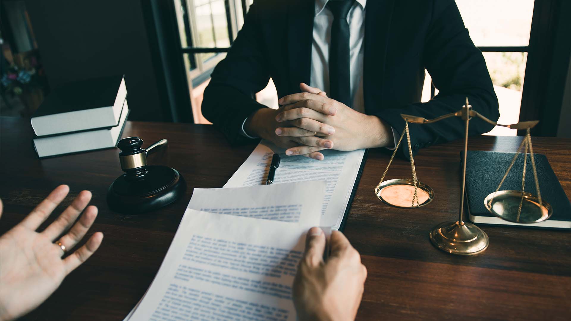 Professional legal consultation with lawyer and client reviewing documents at wooden desk with gavel and scales of justice