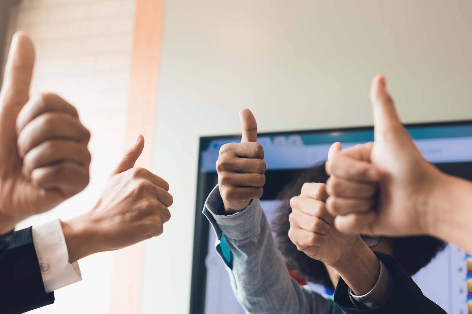 Multiple hands giving thumbs up in front of a computer monitor in an office