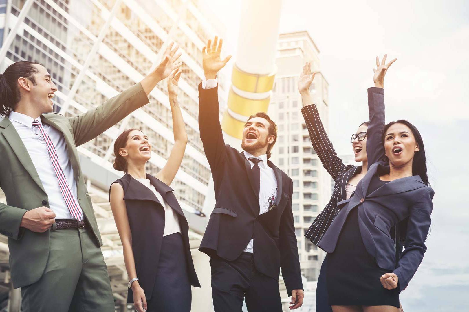 Group of diverse business professionals celebrating with raised hands in front of a city skyline