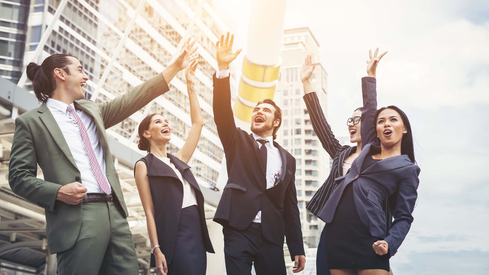 Group of diverse business professionals celebrating with raised hands in front of a city skyline