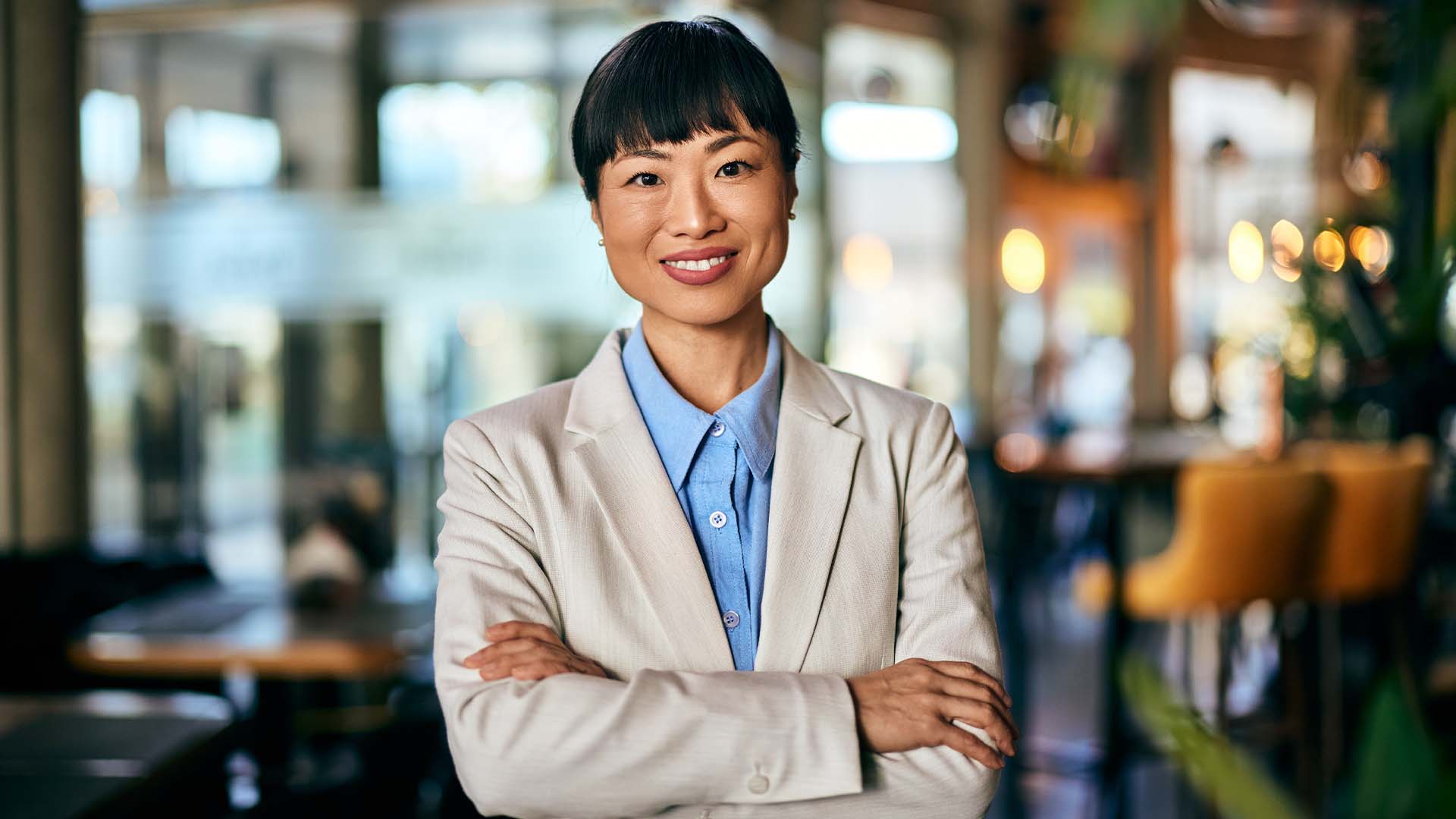 Confident businesswoman with arms crossed smiling in a modern cafe or co-working space