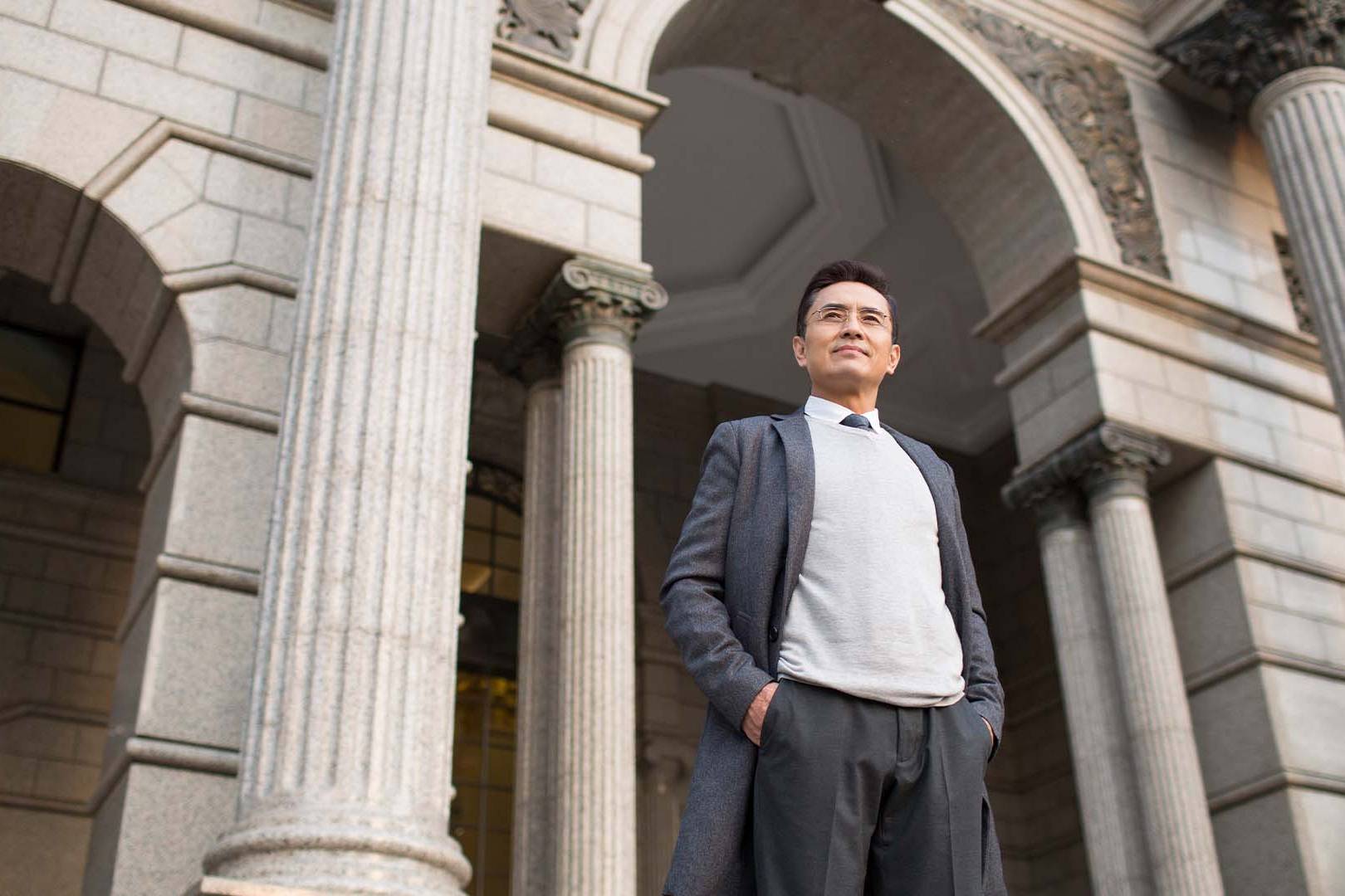 Confident male banking compliance officer standing outside a traditional bank building.