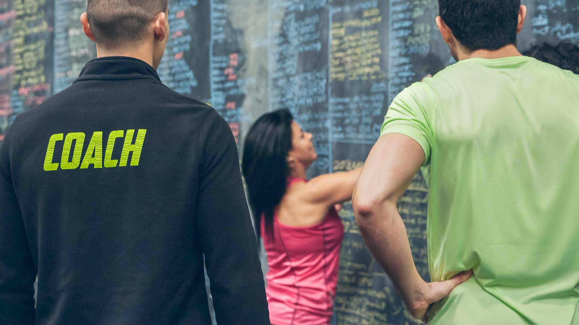 A sports coach wearing a black pullover with COACH in bright green letters observing a training session.