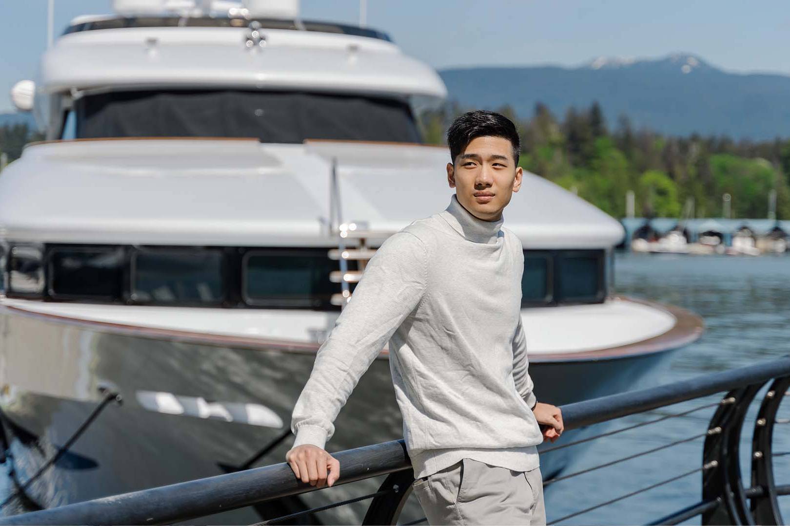 Thoughtful young professional man standing near a luxury yacht representing family office succession stress.
