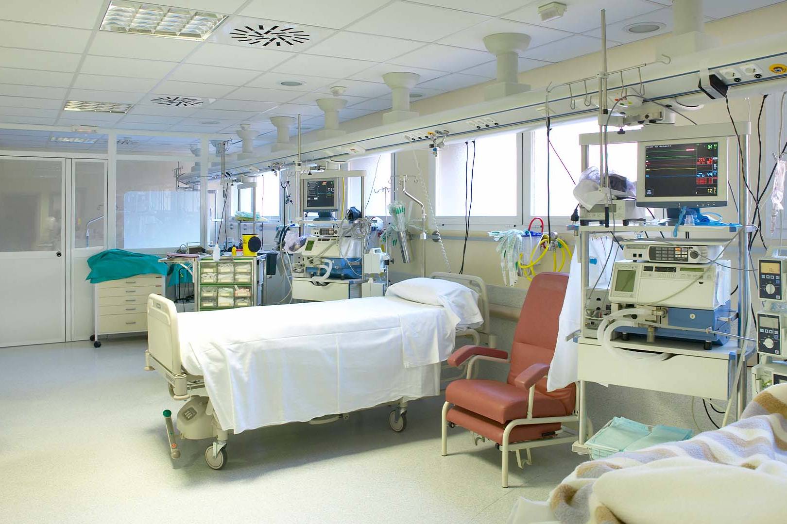 An empty intensive care unit hospital bed surrounded by advanced medical monitors and life support equipment.