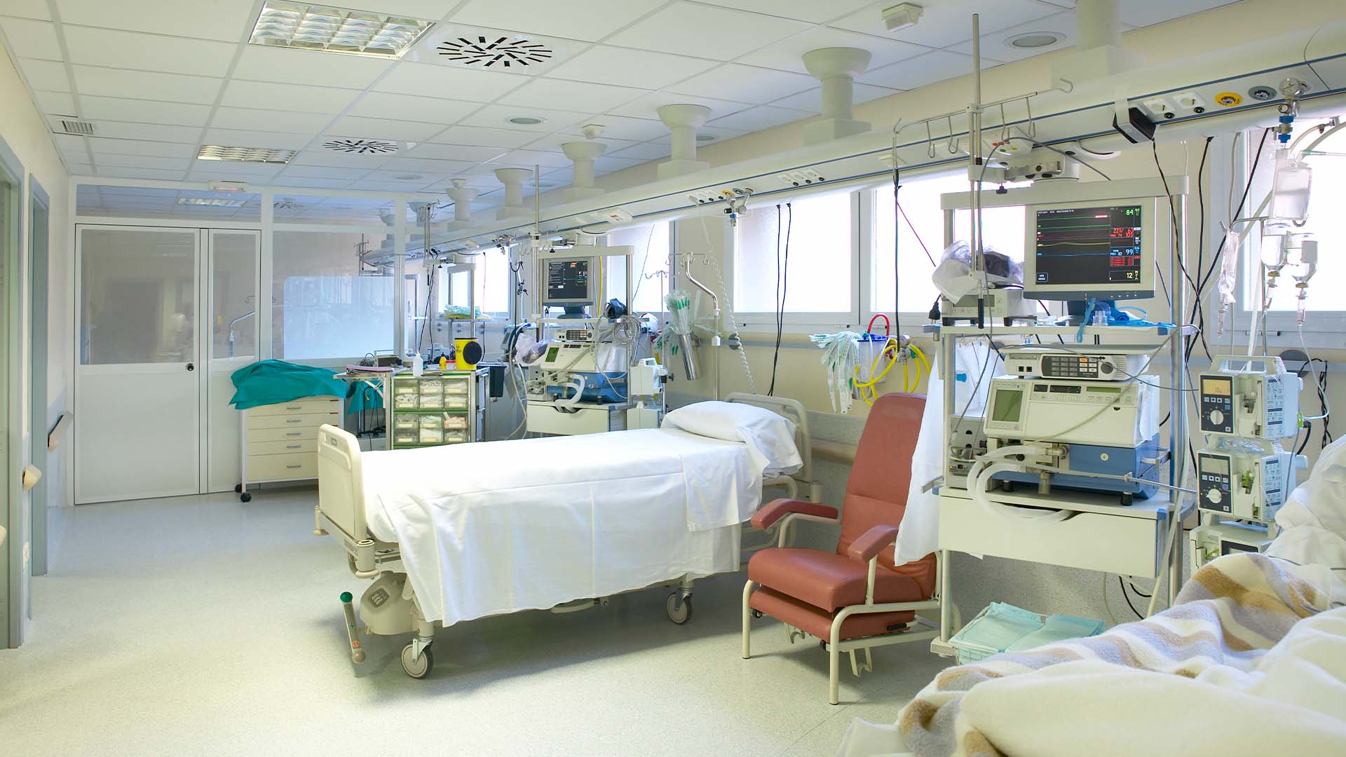An empty intensive care unit hospital bed surrounded by advanced medical monitors and life support equipment.