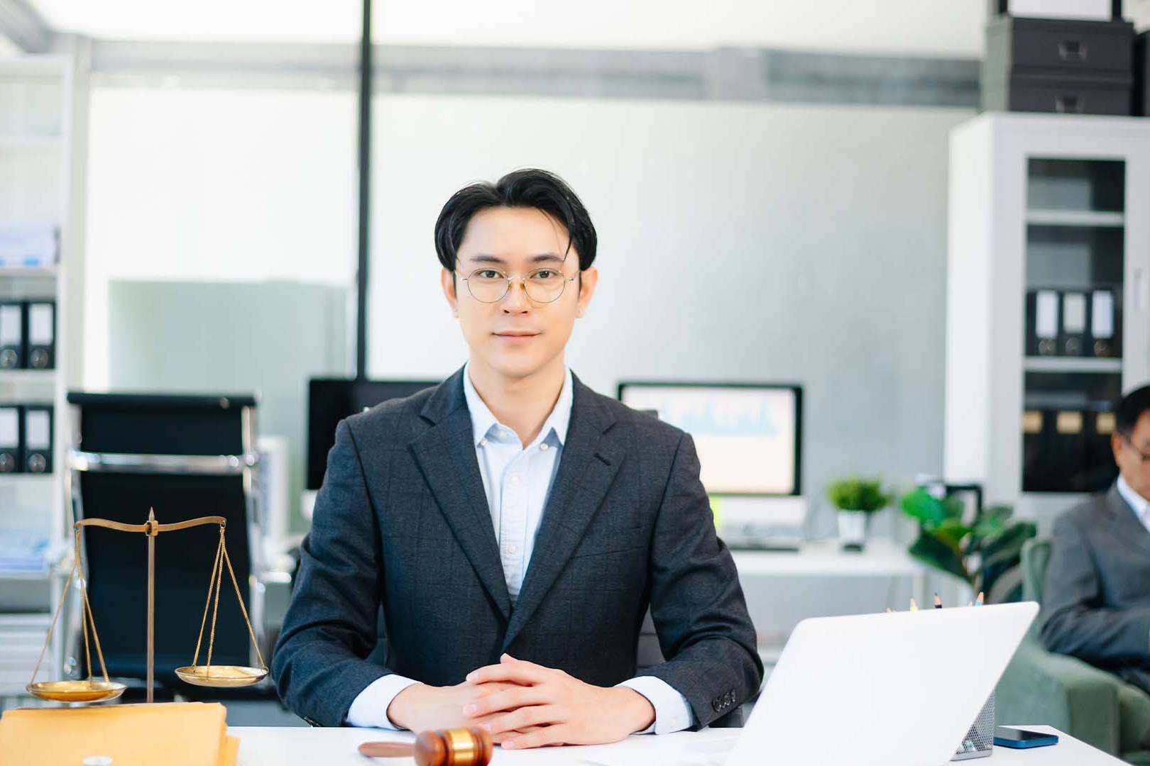 Professional male in-house counsel sitting at a modern office desk with scales of justice.