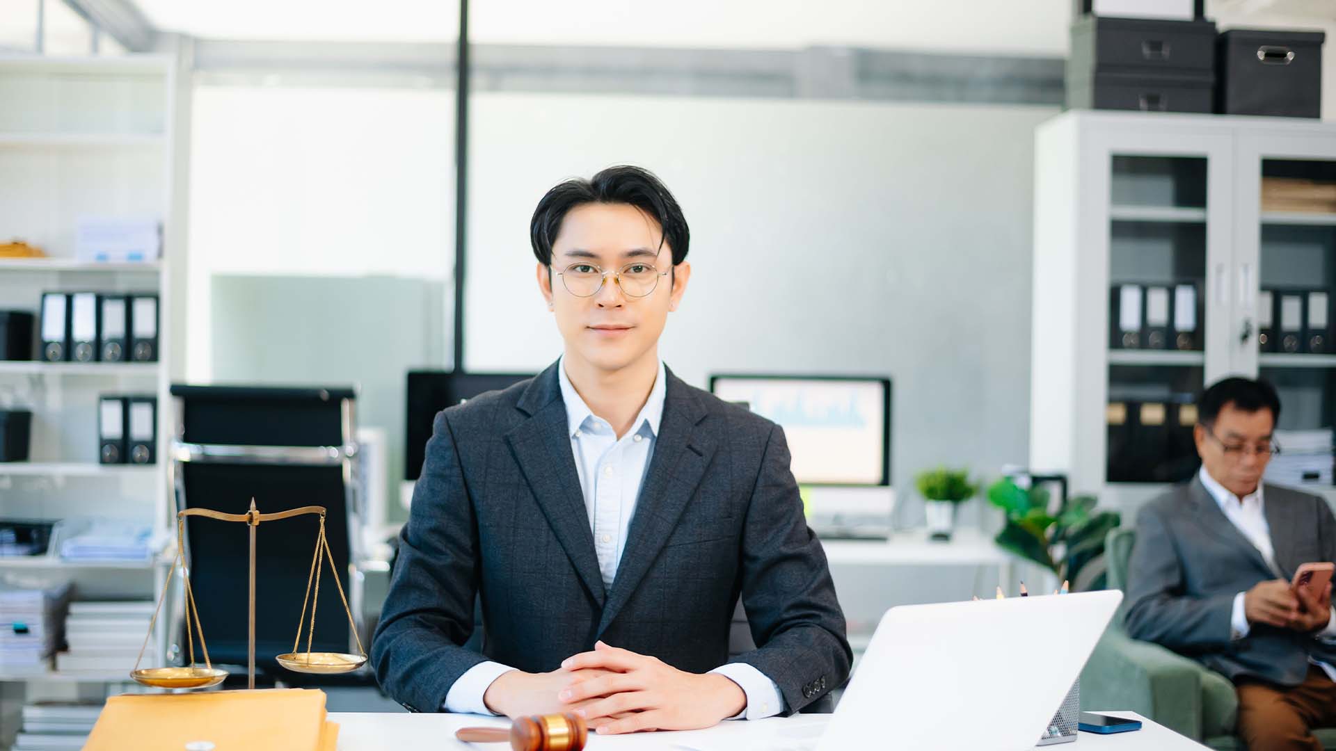 Professional male in-house counsel sitting at a modern office desk with scales of justice.