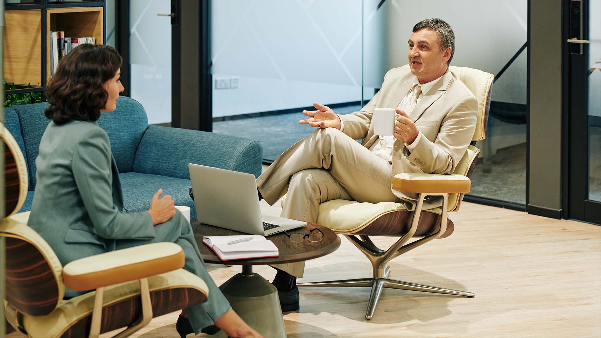 Male executive in a light tan suit talking with a female therapist or consultant in a modern office setting.