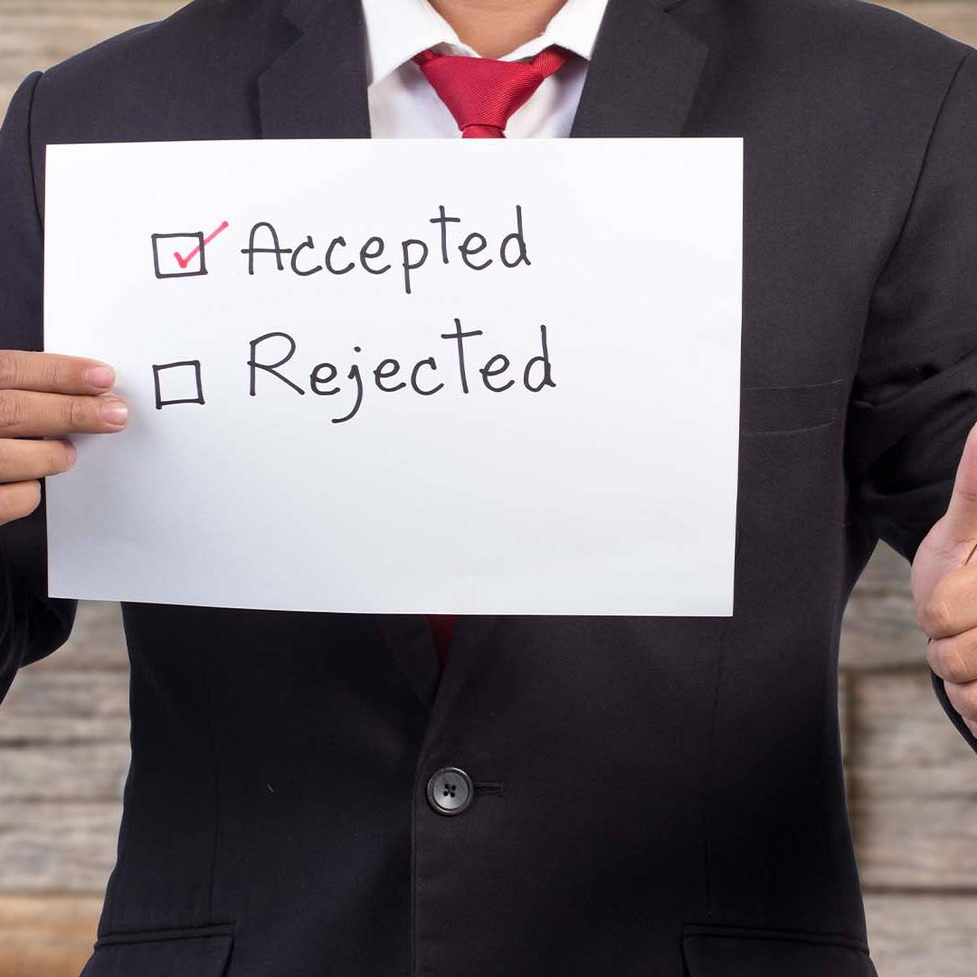 A professional in a dark suit giving a thumbs up while holding a sign with Accepted checked and Rejected unchecked.