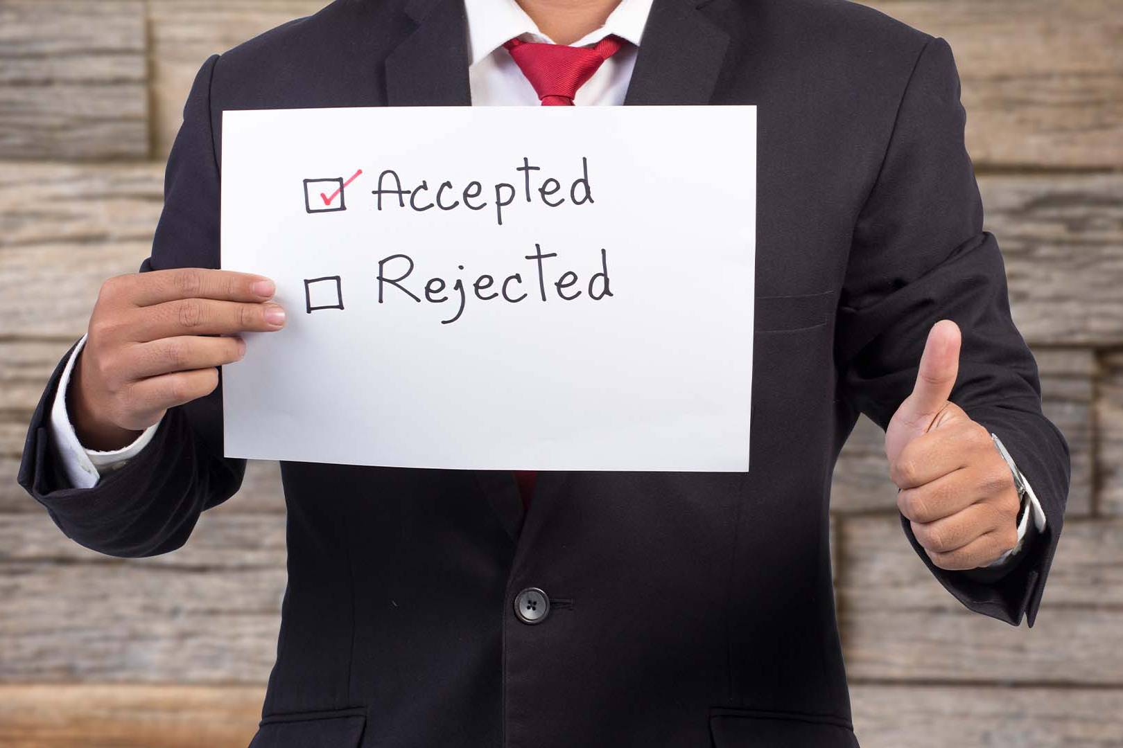 A professional in a dark suit giving a thumbs up while holding a sign with Accepted checked and Rejected unchecked.