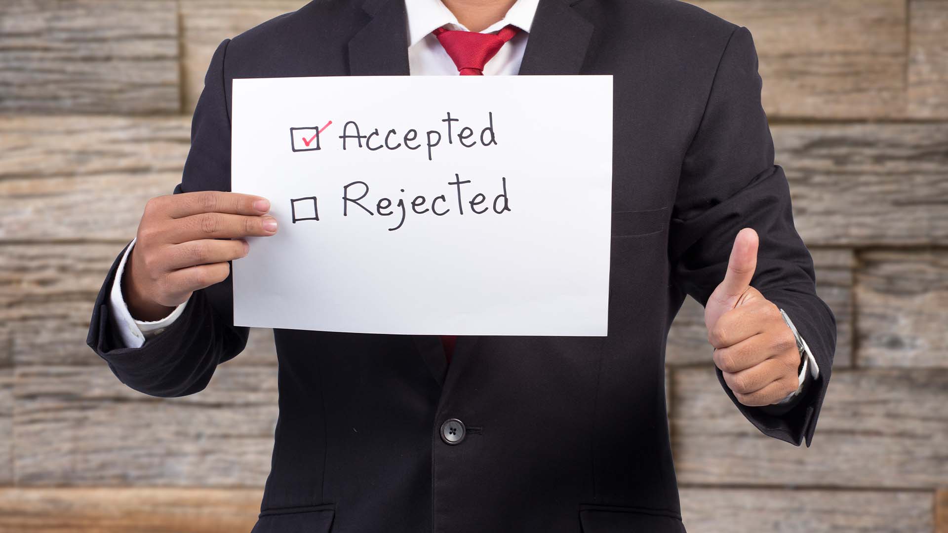 A professional in a dark suit giving a thumbs up while holding a sign with Accepted checked and Rejected unchecked.