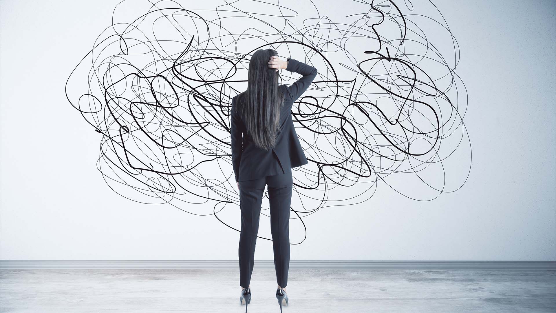 A businesswoman in a dark suit facing a wall covered in a chaotic tangle of black lines.