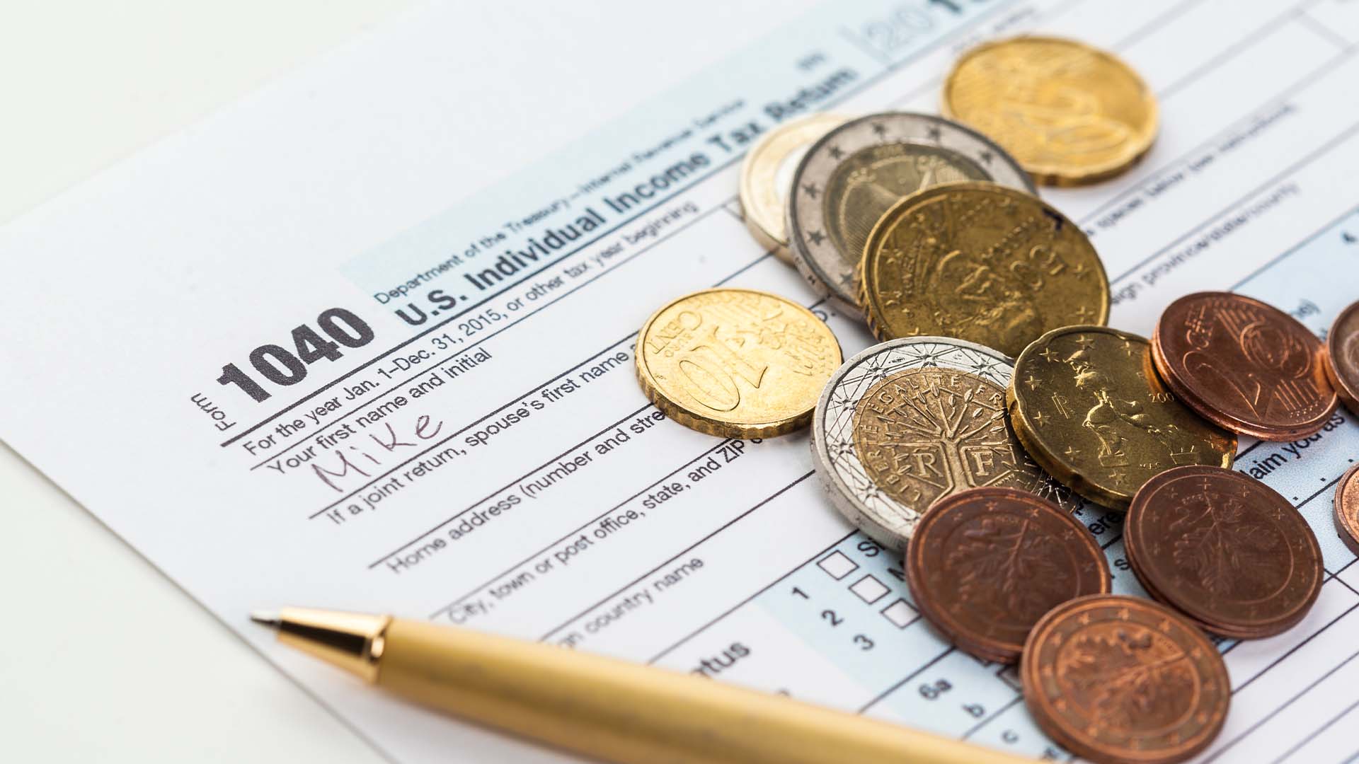 Close-up of a US 1040 tax return form scattered with coins and a pen representing tax partner burnout.