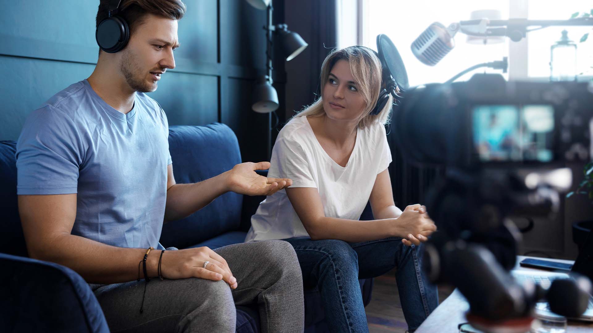 A male and female broadcast producer wearing headphones recording a podcast in front of a professional camera and microphones.