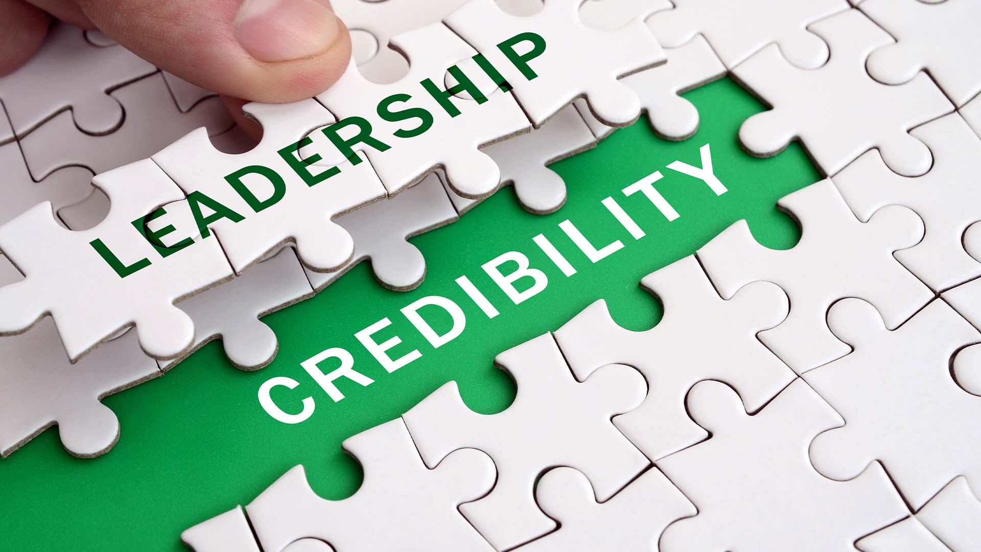 Hand placing a puzzle piece labeled LEADERSHIP over a green space reading CREDIBILITY.